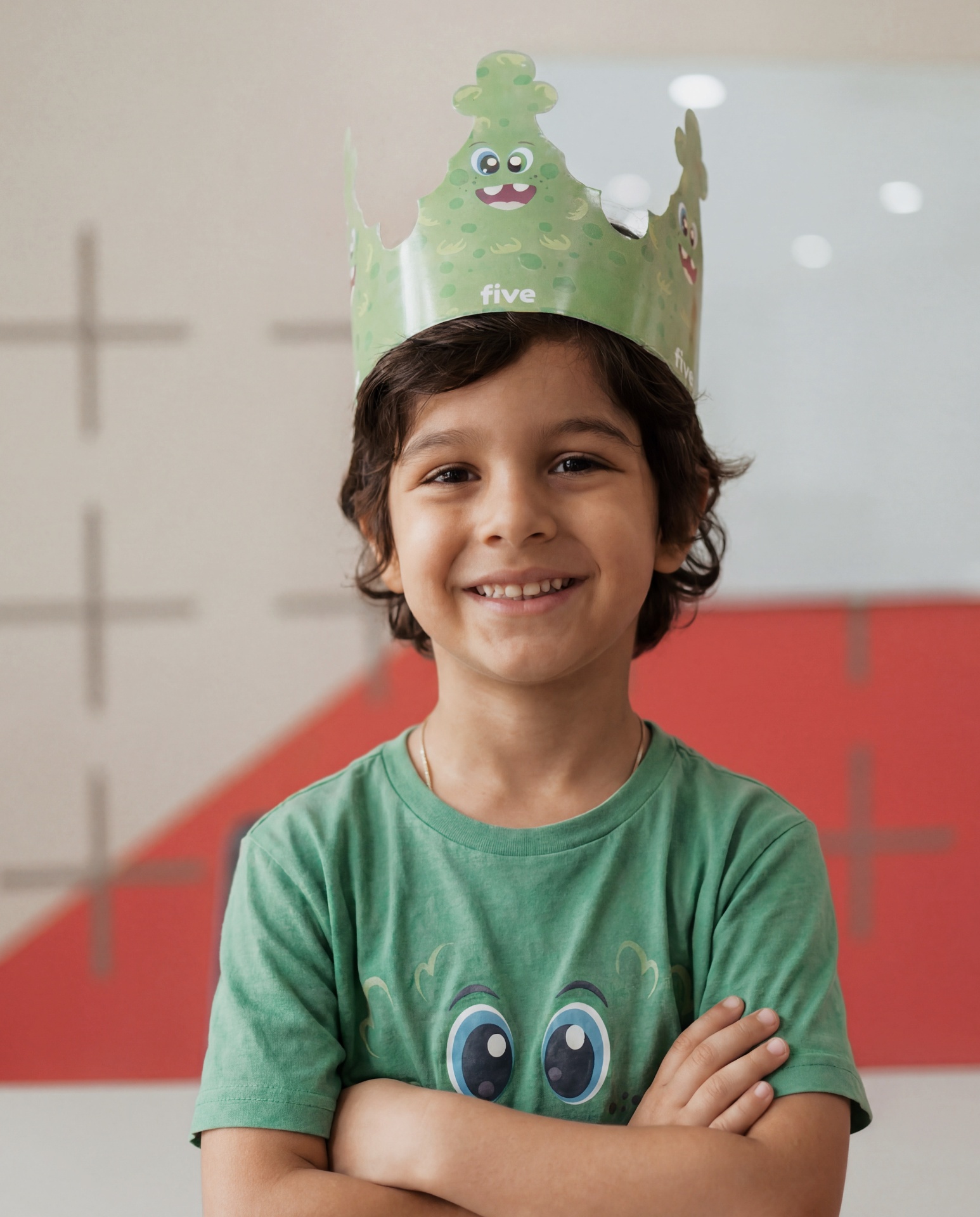 Criança Five sorrindo com coroa verde de monstrinho e camiseta Five